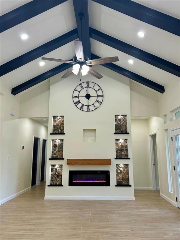 unfurnished living room featuring beamed ceiling, high vaulted ceiling, ceiling fan, a glass covered fireplace, and baseboards