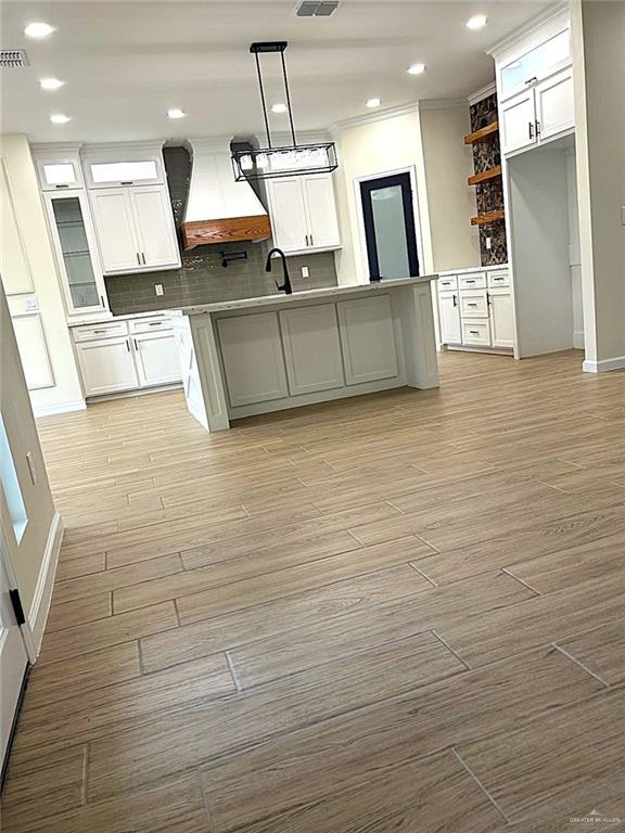 kitchen with white cabinets, custom exhaust hood, light wood-style flooring, and decorative backsplash