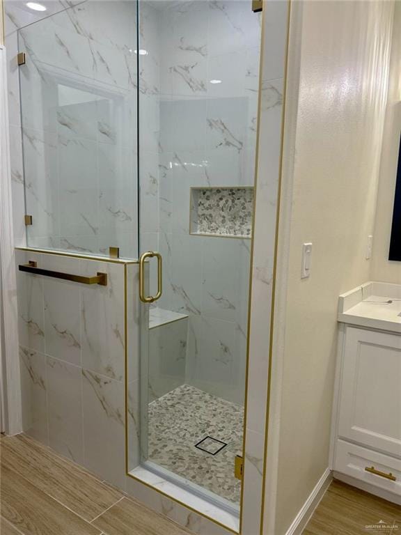 bathroom featuring vanity, a marble finish shower, wood finished floors, and baseboards