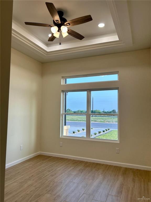 spare room featuring baseboards, light wood-style floors, and a tray ceiling