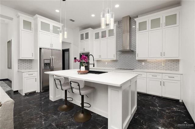 kitchen with black electric cooktop, stainless steel fridge with ice dispenser, marble finish floor, a sink, and wall chimney range hood