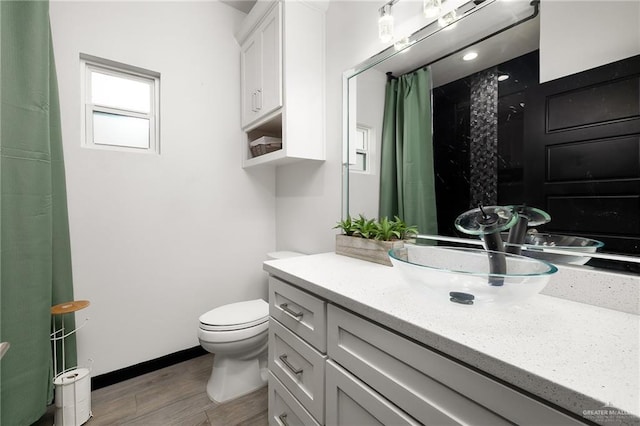 bathroom with toilet, vanity, a shower with curtain, wood finished floors, and baseboards