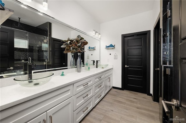bathroom with double vanity, a sink, a shower stall, and wood finished floors