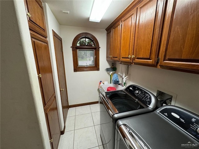 clothes washing area with cabinets, washing machine and dryer, and light tile patterned floors