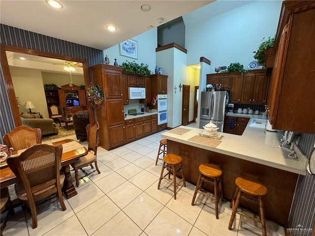 kitchen with a breakfast bar, light tile patterned flooring, white appliances, and kitchen peninsula