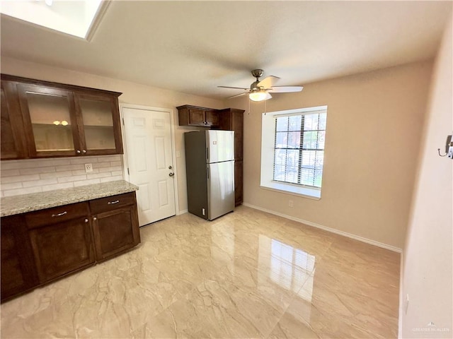 kitchen featuring decorative backsplash, light stone counters, dark brown cabinetry, and stainless steel refrigerator