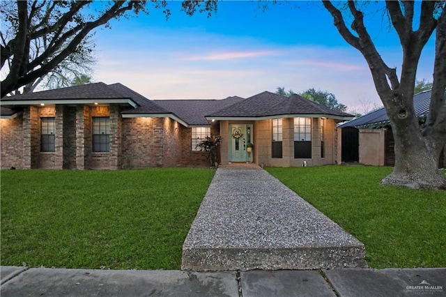 view of front facade with brick siding, roof with shingles, and a front yard