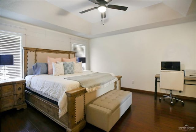 bedroom featuring a tray ceiling, dark wood-style flooring, ceiling fan, and baseboards