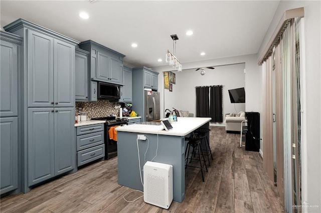 kitchen featuring hardwood / wood-style floors, an island with sink, decorative light fixtures, a kitchen bar, and appliances with stainless steel finishes