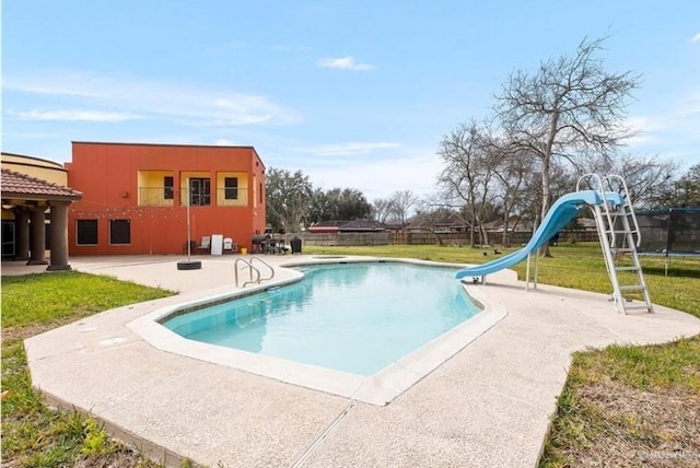 view of pool featuring a lawn, a trampoline, a patio, and a water slide