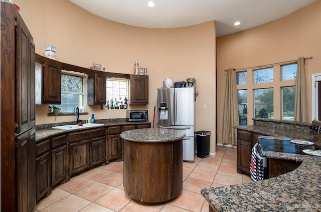 kitchen featuring sink, dark stone countertops, light tile patterned floors, appliances with stainless steel finishes, and a kitchen island