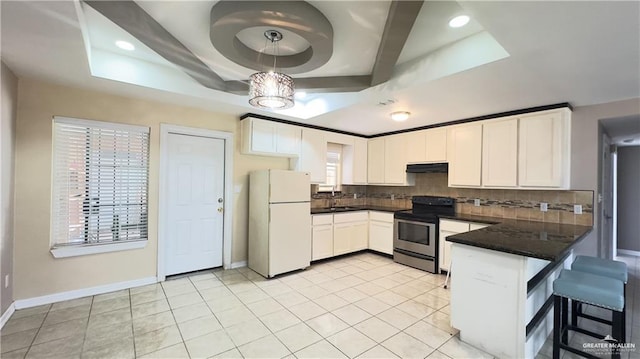 kitchen featuring under cabinet range hood, a peninsula, freestanding refrigerator, dark countertops, and stainless steel range with electric stovetop