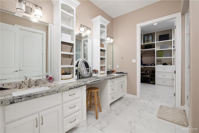 full bath featuring double vanity, marble finish floor, a walk in closet, and a sink