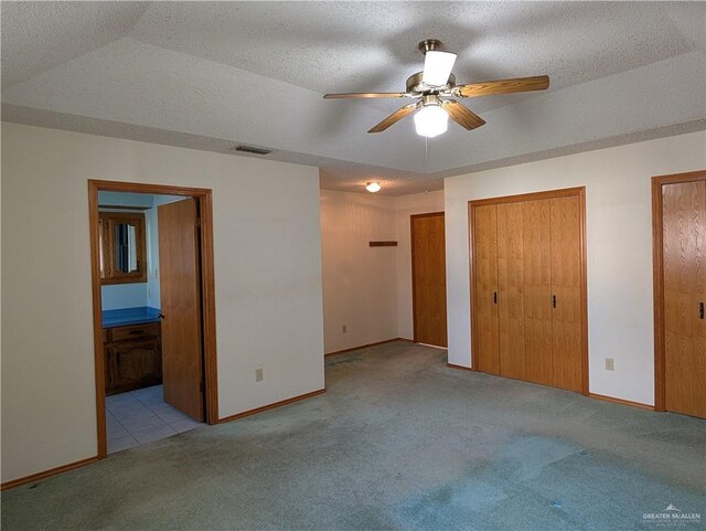 unfurnished bedroom with carpet, multiple closets, baseboards, ensuite bath, and a textured ceiling