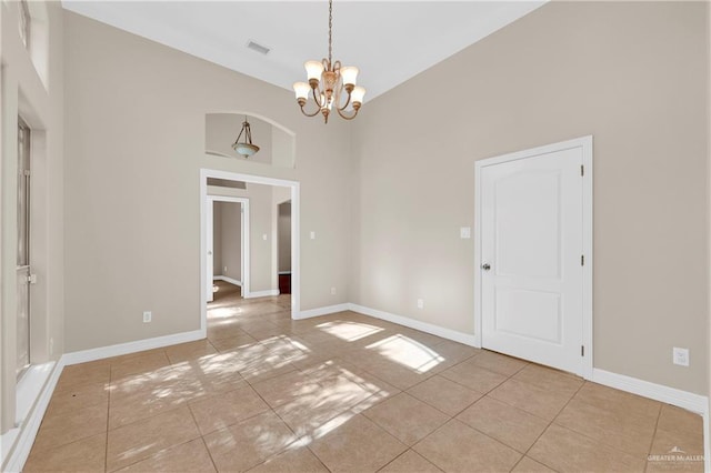 empty room with a notable chandelier, a high ceiling, and light tile patterned floors