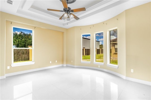 tiled empty room with a raised ceiling, plenty of natural light, and ornamental molding