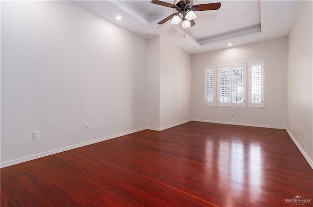 spare room with dark hardwood / wood-style flooring, a raised ceiling, and ceiling fan