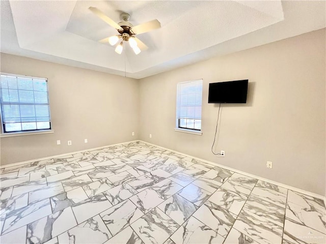 empty room with ceiling fan and a raised ceiling