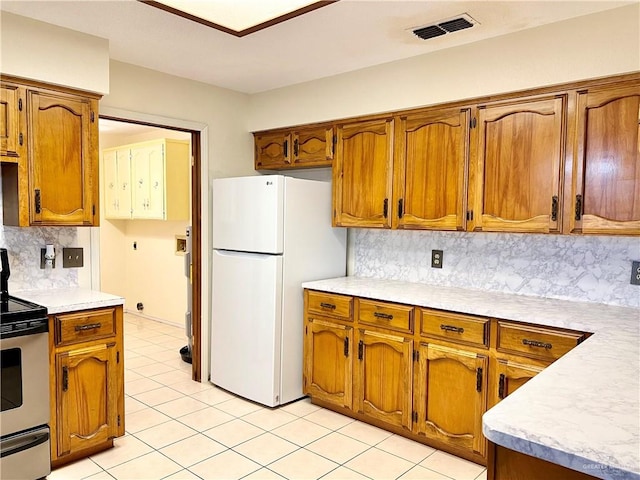 kitchen featuring stainless steel electric stove, backsplash, white fridge, and light tile patterned floors