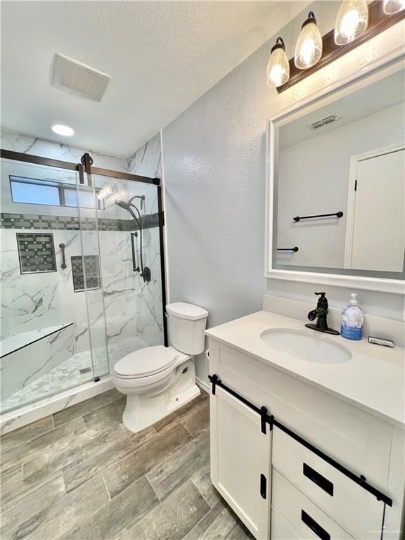 bathroom featuring vanity, toilet, a shower with shower door, and a textured ceiling