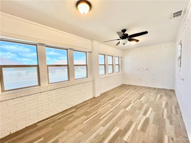 spare room featuring ceiling fan, crown molding, brick wall, and hardwood / wood-style flooring