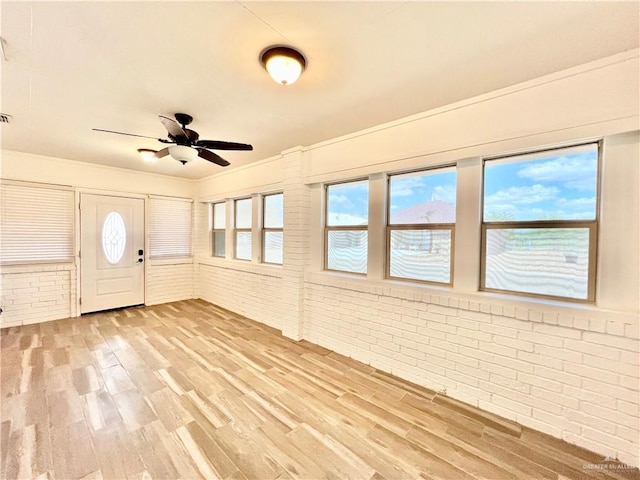 entrance foyer with hardwood / wood-style floors, ceiling fan, and brick wall