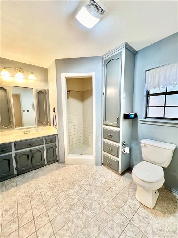 bathroom with tiled shower, tile patterned flooring, vanity, and toilet