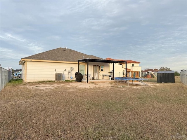 rear view of house featuring cooling unit, a lawn, and a trampoline