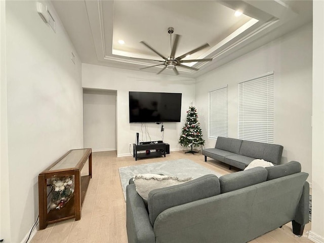 living room featuring a raised ceiling, ceiling fan, and light wood-type flooring