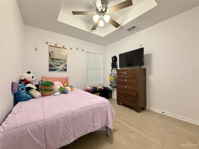 bedroom featuring a raised ceiling, ceiling fan, and light wood-type flooring