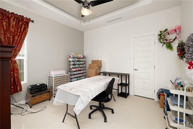 office space with a tray ceiling, visible vents, light tile patterned flooring, and ceiling fan
