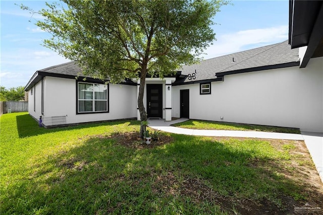 view of front of property with stucco siding, fence, roof with shingles, and a front yard