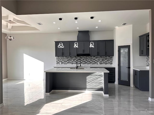 kitchen with decorative light fixtures, sink, decorative backsplash, and an island with sink