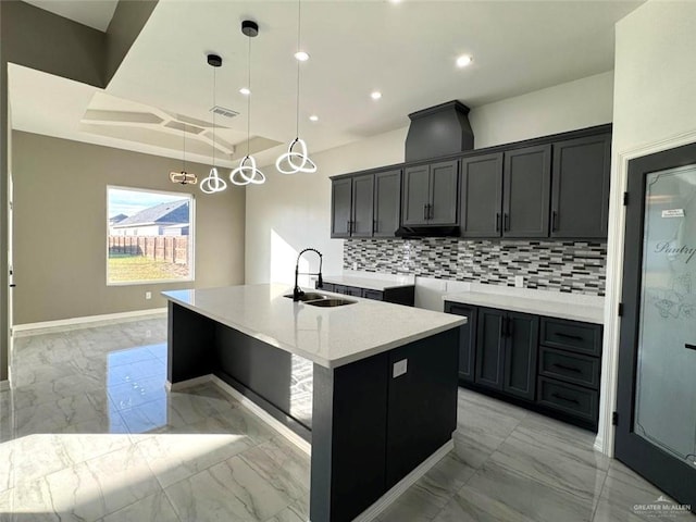 kitchen with decorative light fixtures, a center island with sink, decorative backsplash, sink, and a tray ceiling