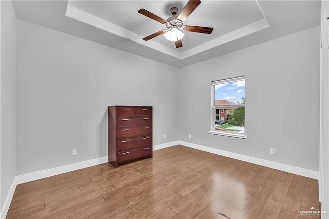 unfurnished room featuring ceiling fan, light hardwood / wood-style flooring, and a tray ceiling