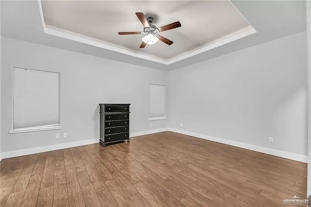 empty room with hardwood / wood-style floors, a raised ceiling, and ceiling fan