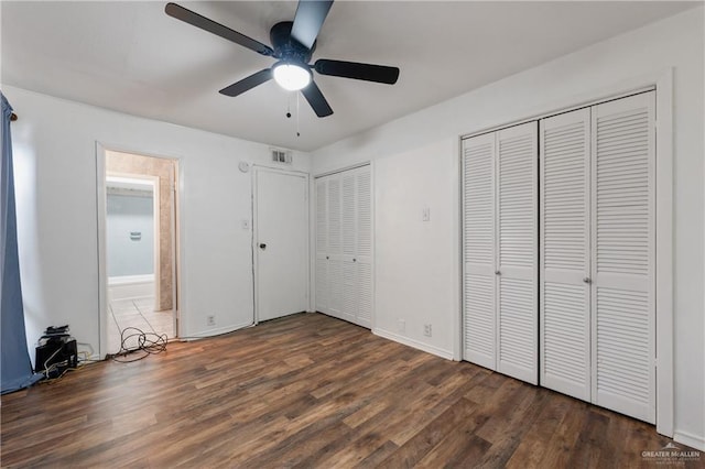 unfurnished bedroom with dark hardwood / wood-style flooring, multiple closets, and ceiling fan