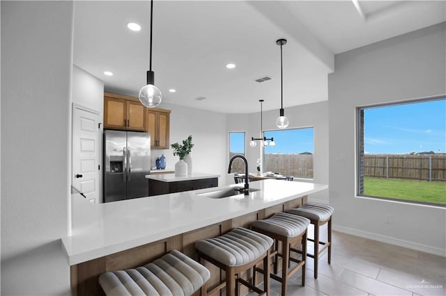 1502 Stirrup Cir, San Benito, TX 78586 - kitchen with stainless steel fridge with ice dispenser, brown cabinetry, a kitchen island, a breakfast bar area, and recessed lighting