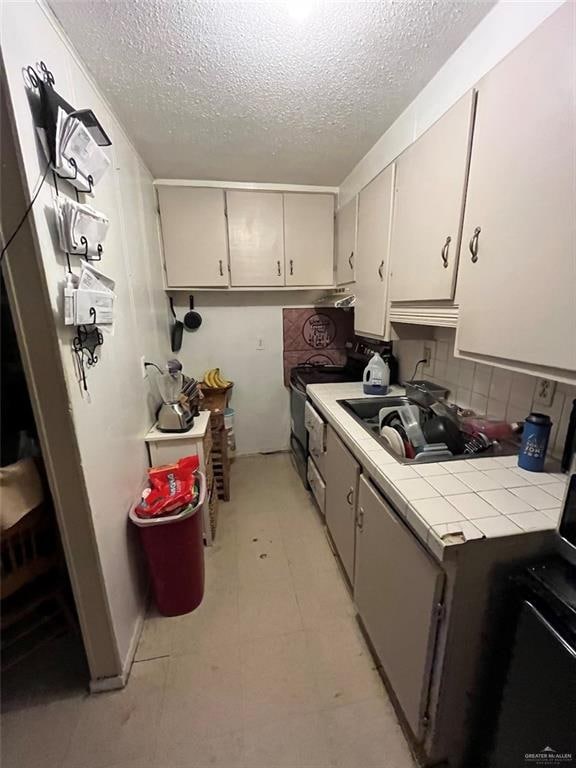 kitchen featuring sink, black range with electric cooktop, tile countertops, a textured ceiling, and decorative backsplash