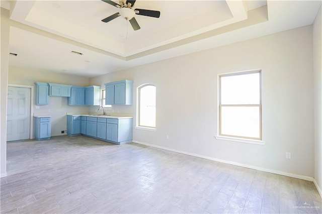 kitchen with a tray ceiling, ceiling fan, sink, and light hardwood / wood-style floors