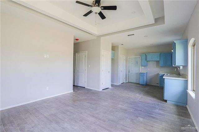 kitchen with sink, ceiling fan, blue cabinetry, a tray ceiling, and light hardwood / wood-style floors