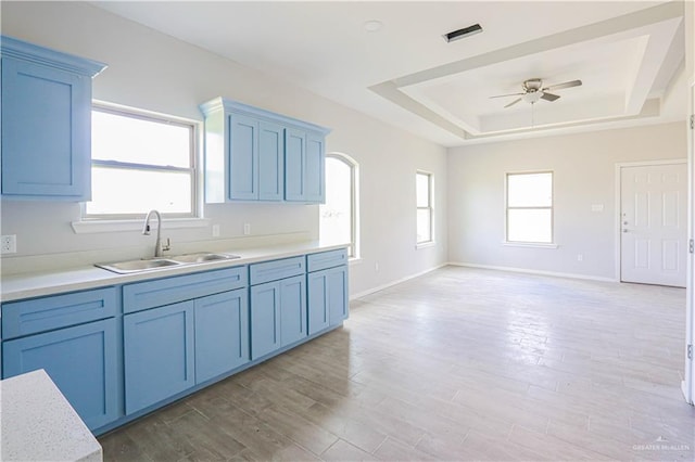 kitchen featuring a raised ceiling, sink, ceiling fan, blue cabinetry, and light hardwood / wood-style floors