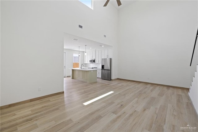 1214 N Lincoln Ave, San Juan, TX 78589 - unfurnished living room featuring ceiling fan, light wood-style floors, baseboards, a high ceiling, and a sink