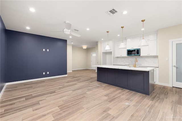 3409 Emma Dr, Weslaco, TX 78596 - kitchen with stainless steel microwave, visible vents, white cabinetry, light countertops, and light wood-style floors