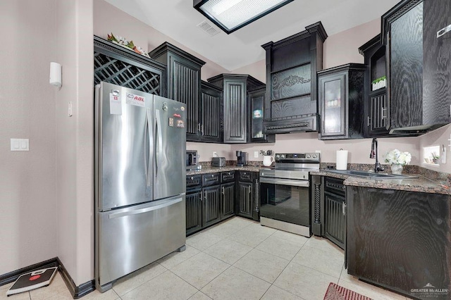 3908 Hill Crest Dr, Mission, TX 78573 - kitchen featuring stainless steel appliances, dark cabinets, light tile patterned floors, dark stone counters, and glass insert cabinets