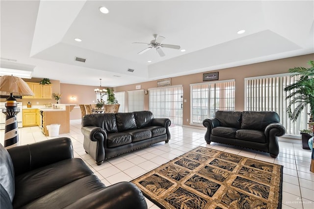 living room featuring light tile patterned floors, ceiling fan with notable chandelier, and a tray ceiling