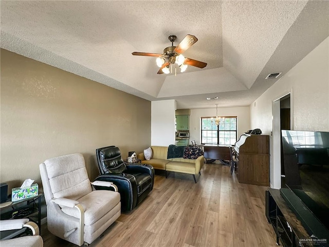 living area with visible vents, ceiling fan with notable chandelier, a tray ceiling, a textured ceiling, and light wood finished floors