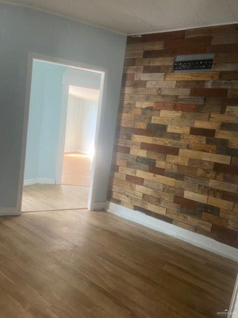 empty room featuring baseboards, light wood-style flooring, and wood walls