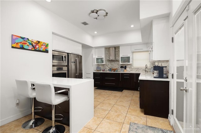 kitchen with appliances with stainless steel finishes, backsplash, wall chimney exhaust hood, dark brown cabinets, and white cabinets