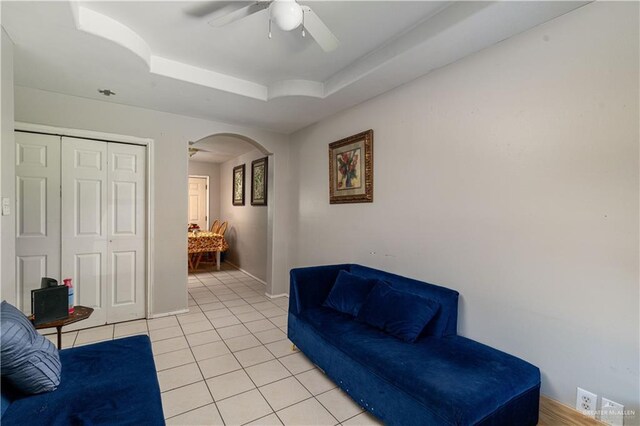 living area with ceiling fan, light tile patterned floors, and a tray ceiling